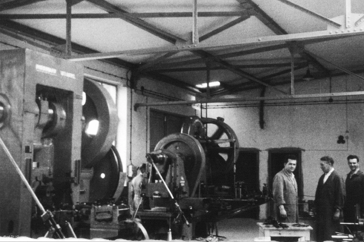 Parte di un capannone industriale con alcune macchine a sinistra e tre uomini che chiacchierano a destra © ABUS