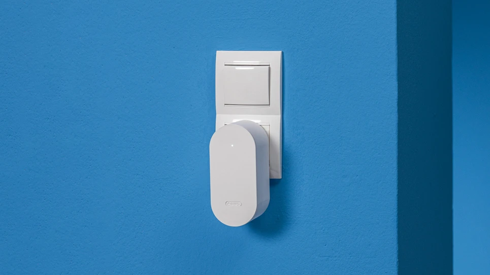 PONT Un en blanc branché dans une prise sur un mur bleu © ABUS