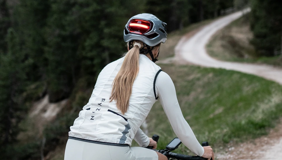 Vue arrière d'une femme sur un vélo de gravel avec le casque de vélo de gravel Taipan LED. Le feu arrière s'allume en rouge. © ABUS