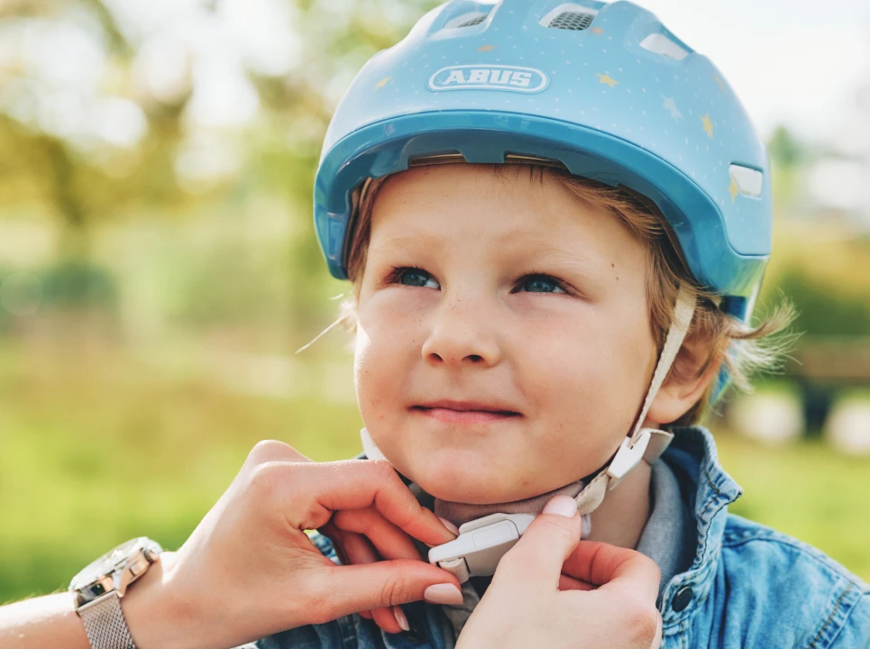 Kind mit ABUS Smiley 3.0 Fahrradhelm in der Farbe Pure Bluestars, während der Kinnverschluss Fidlock des Helms geschlossen wird © ABUS
