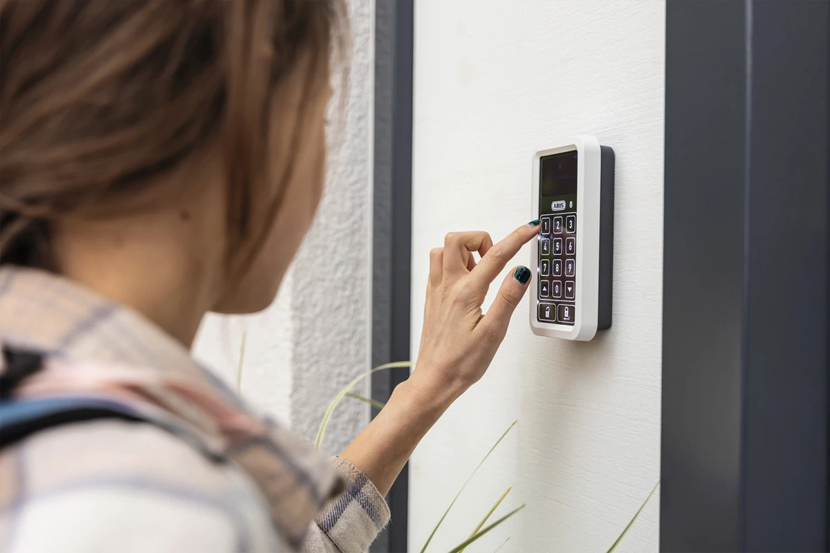 Une jeune fille tape un code sur un clavier ABUS One pour ouvrir sa porte d'entrée © ABUS