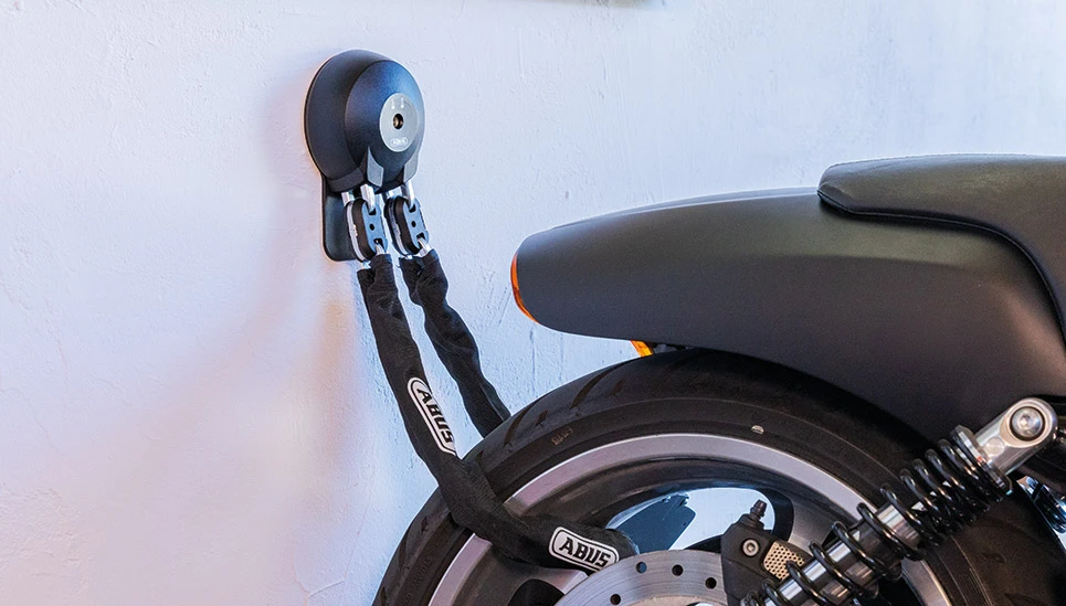 Het achterwiel van een motor wordt in een garage vastgezet met een ketting aan een muur-grondanker. ©ABUS