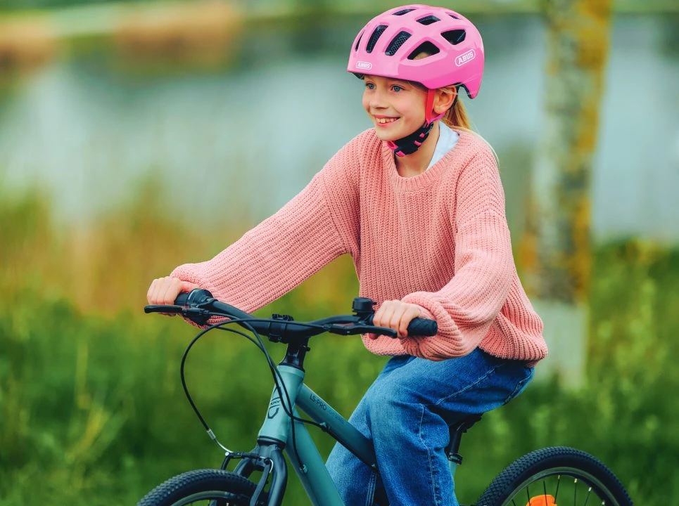 A girl is riding a bike and smiling; she is wearing the pink YOUN-I 3.0 cycle helmet © ABUS