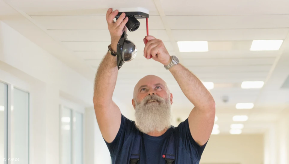 Ein Handwerker montiert eine Kamera an der Decke. © ABUS