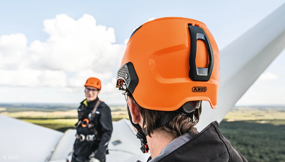 Zwei Männer auf einem Windrad, beide ausgerüstet mit orangefarbenen ABUS-Helmen und weiterer persönlicher Schutzausrüstung. © ABUS