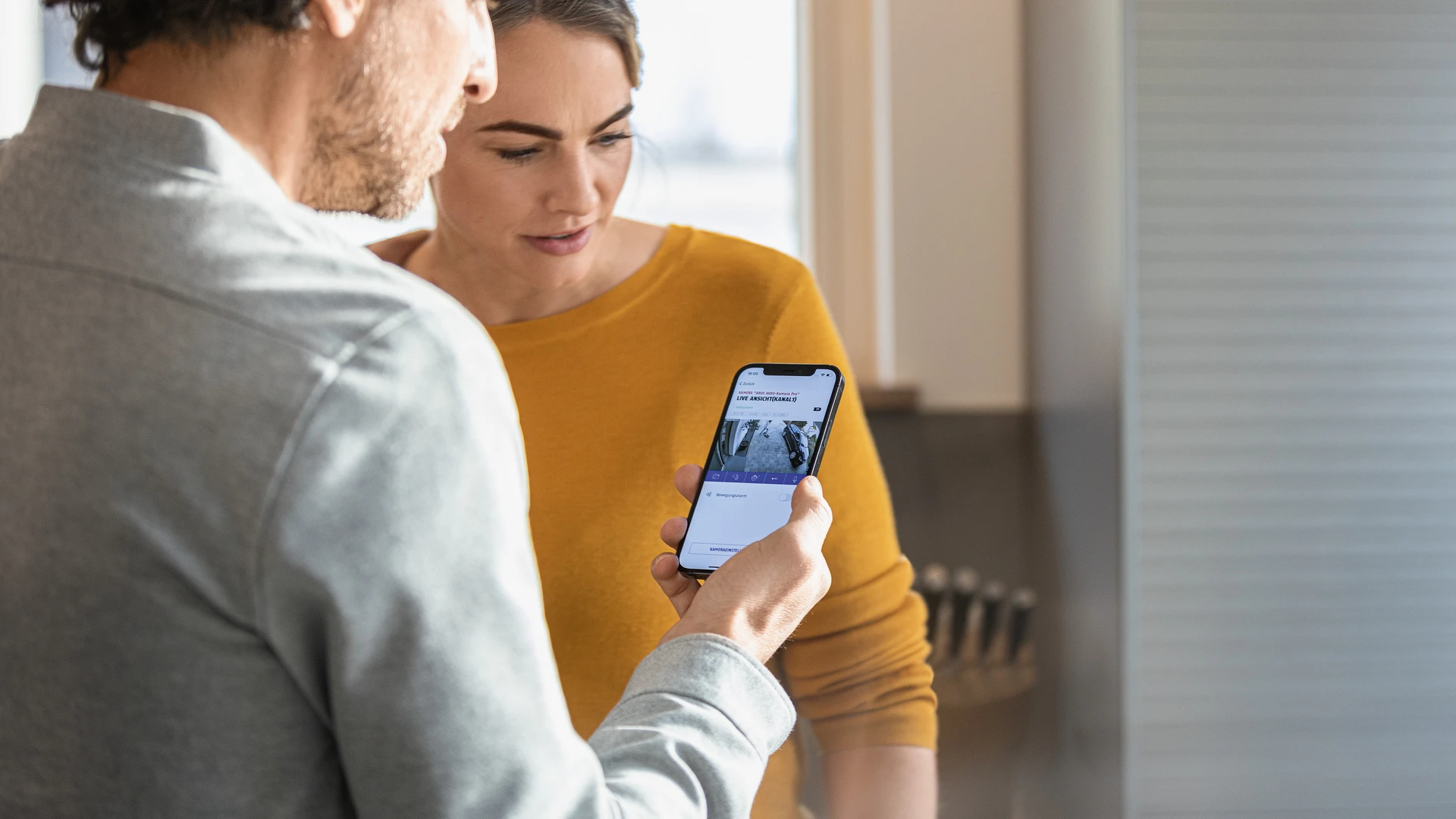 Ein Paar schaut auf ein Smartphone in der Hand des Mannes. Auf dem Display sind Live-Bilder der Akku Kamera Pro zu sehen.