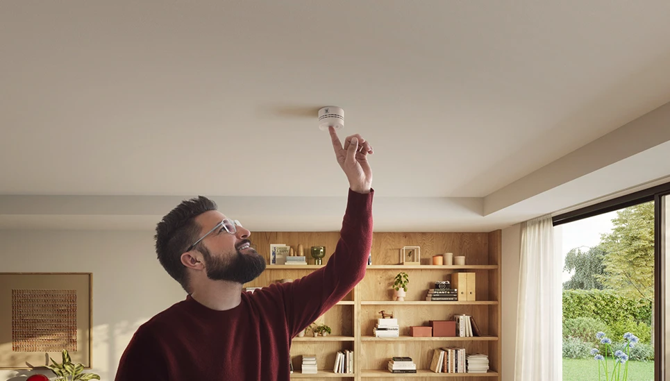 Un uomo preme un pulsante sul rilevatore di fumo PREFIRA SMART montato sul soffitto © ABUS