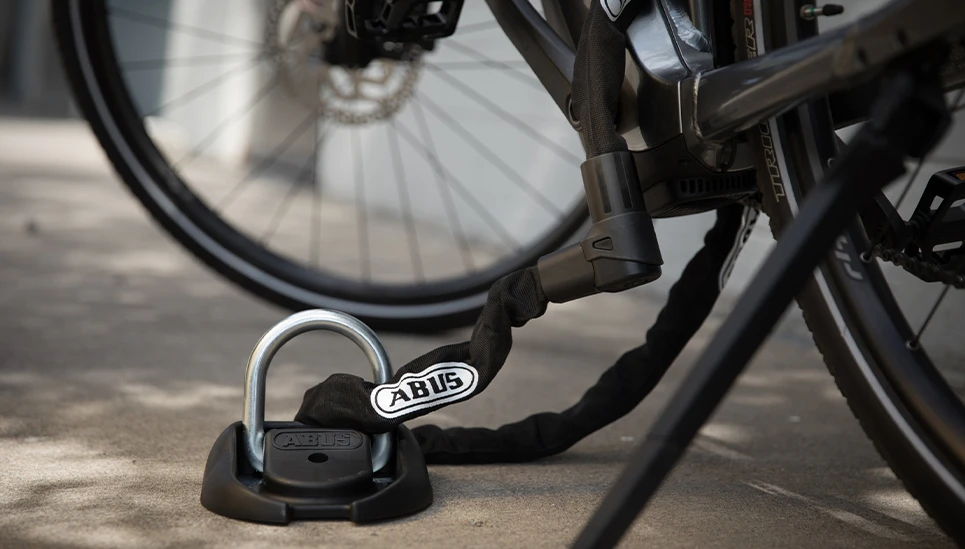 ABUS Wand-Bodenanker 100 mit einem ABUS Kettenschloss verbunden am Fahrrad gesichert ©ABUS