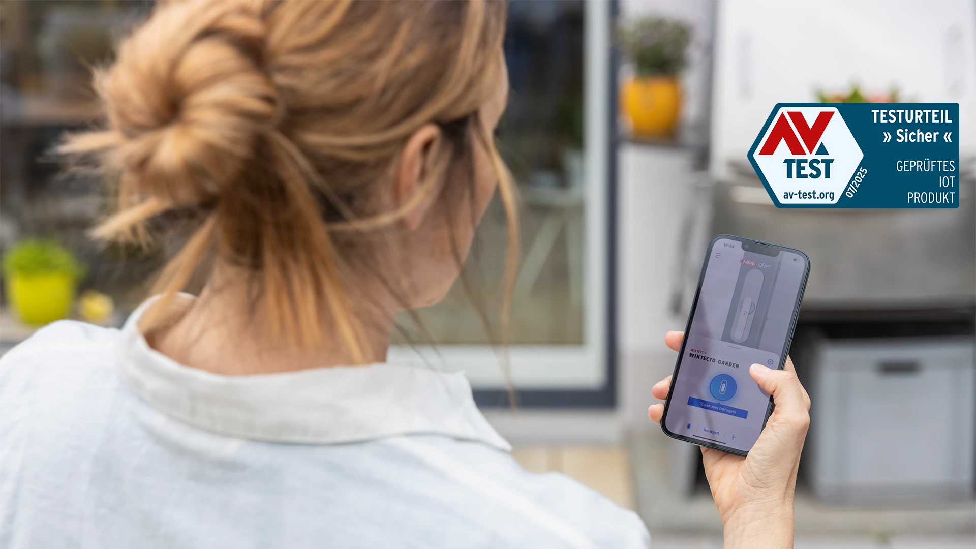 Eine Frau mit der ABUS One App auf ihrem Smartphone und dem AV Test Siegel © ABUS