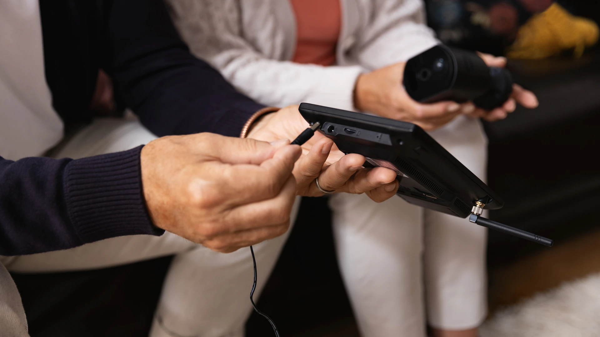 Ein Mann hält den Monitor des ABUS EasyLook Basicsets in der linken Hand, mit der rechten steckt er an der Rückseite des Monitors ein Kabel ein.