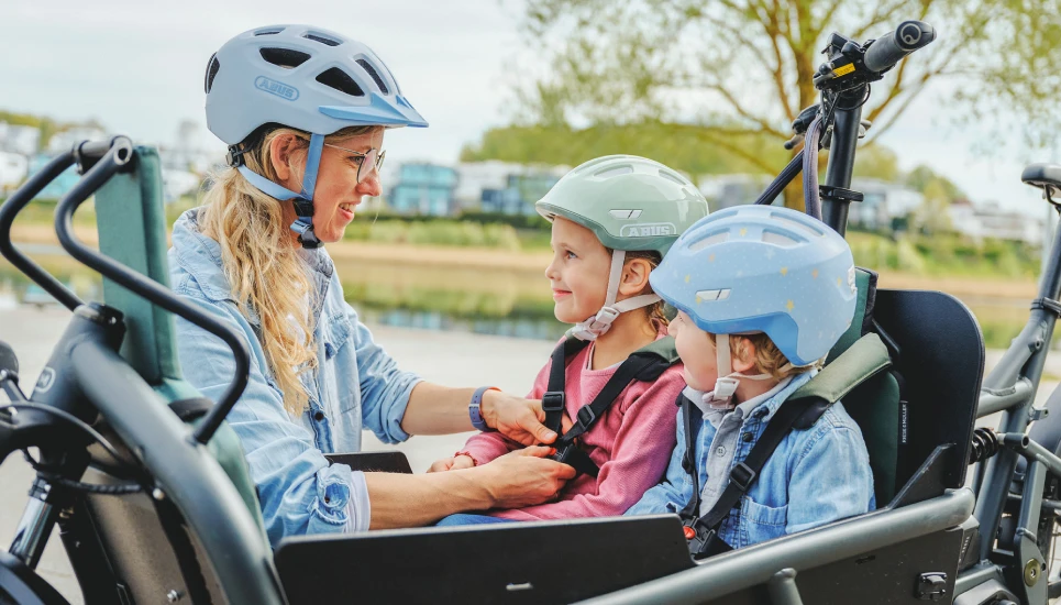 Mutter schnallt Kinder im Lastenfahrrad an © ABUS