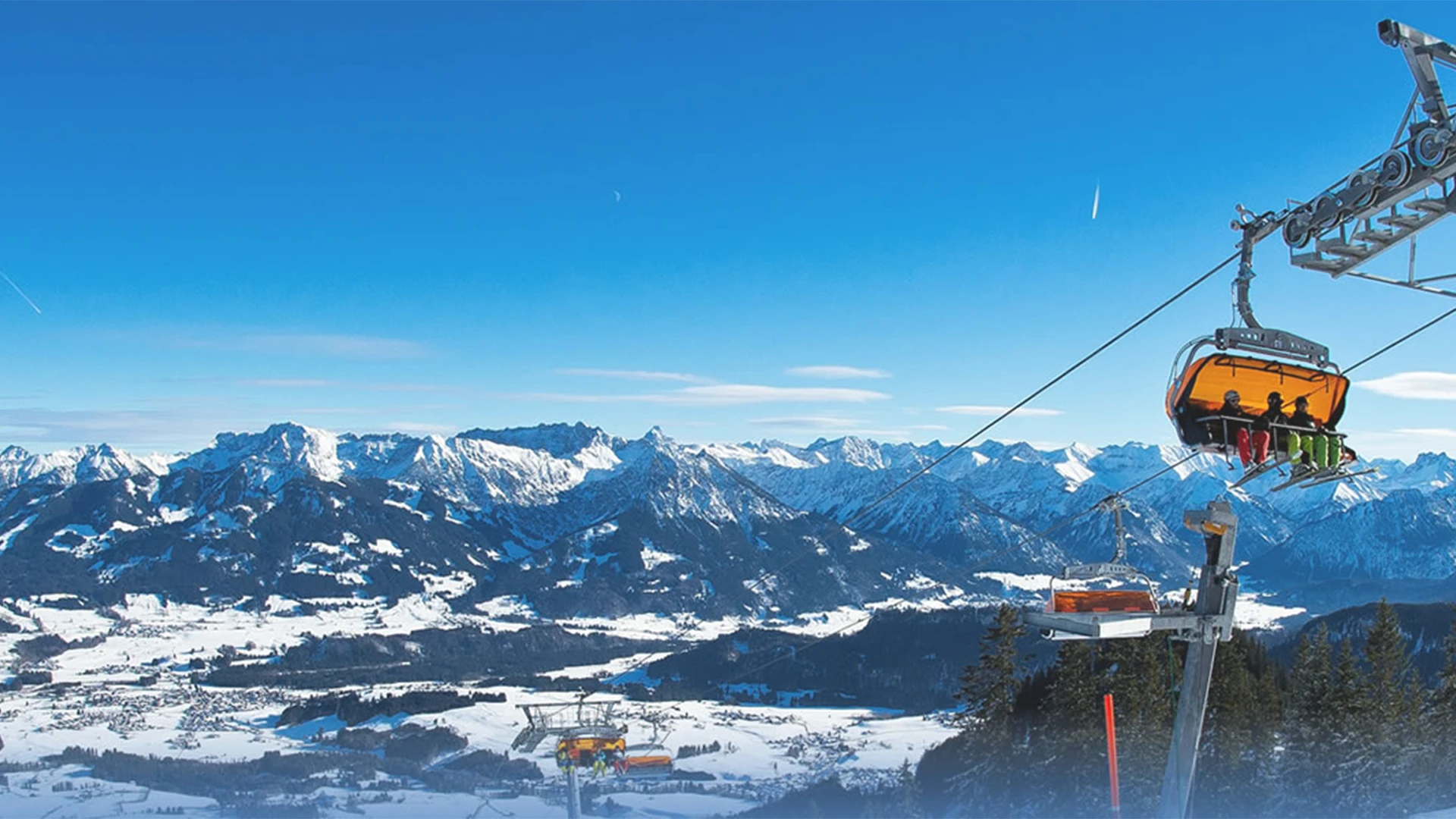 Sessellift vor schneebedeckten Alpen unter blauem Himmel.