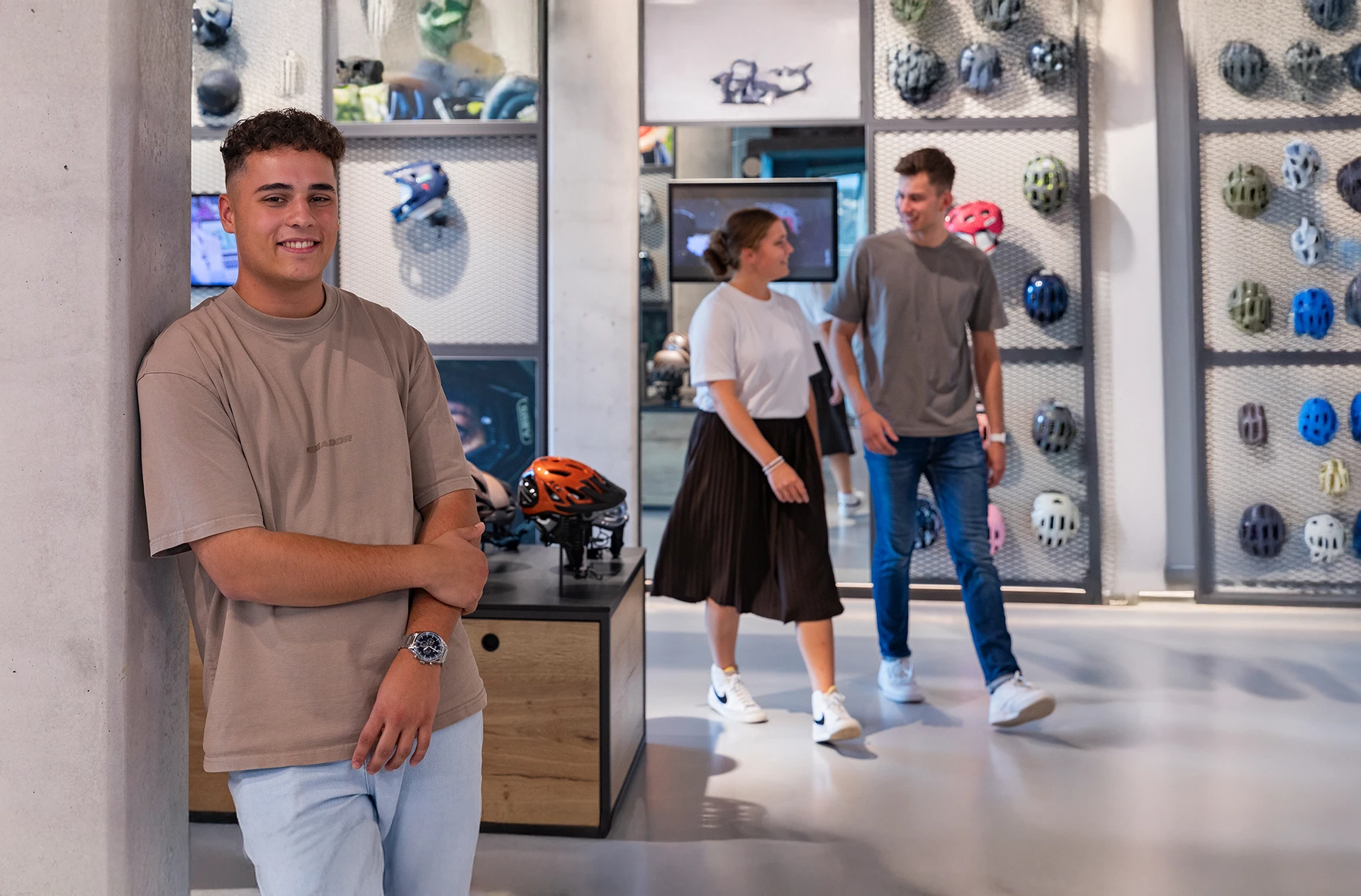 Auszubildender im ABUS Showroom vor einer Helm-Ausstellung, Kolleg:innen im Hintergrund © ABUS