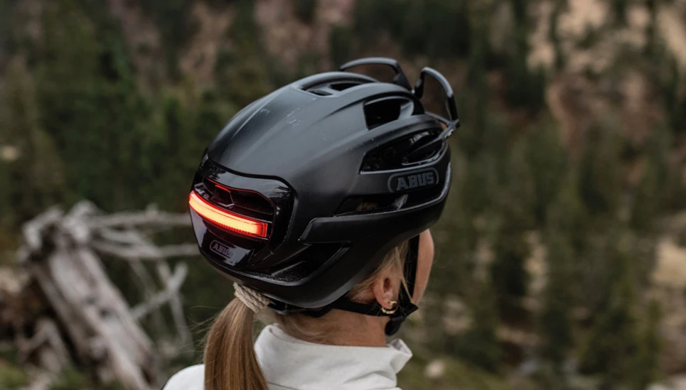 Close-up of a woman wearing a Taipan LED gravel bike helmet in black from behind; helmet rear light glows red © ABUS