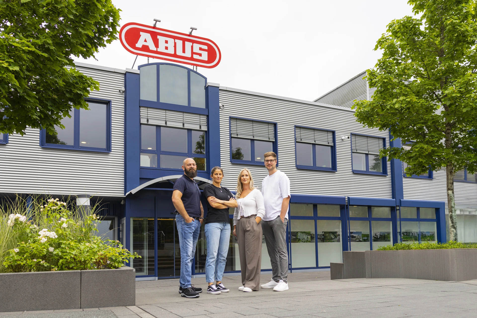 Vier Mitarbeitende vor dem ABUS-Standort Rehe mit Firmengebäude und ABUS-Logo im Hintergrund © ABUS