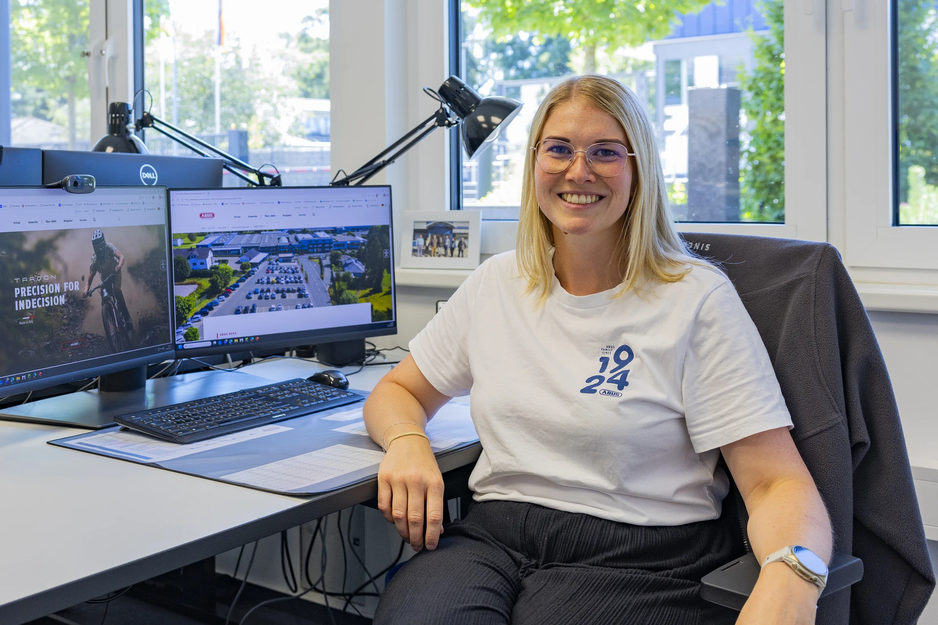 Mitarbeiterin sitzt am Schreibtisch im Büro und lächelt freundlich in die Kamera © ABUS