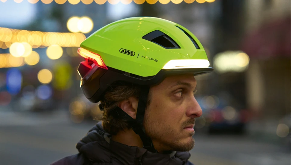 Mann mit urban Fahrradhelm HYP-E in Signal Yellow mit Front- und Rücklicht im Stadtverkehr bei Dämmerung © ABUS