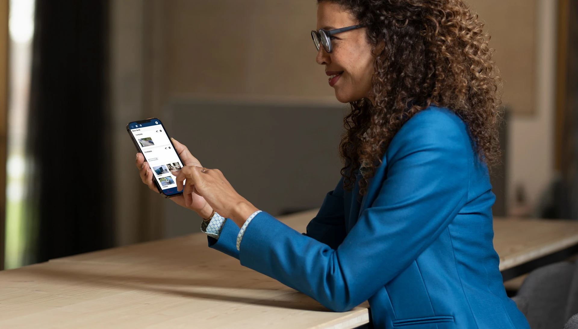 Frau an Schreibtisch mit Smartphone in der Hand.