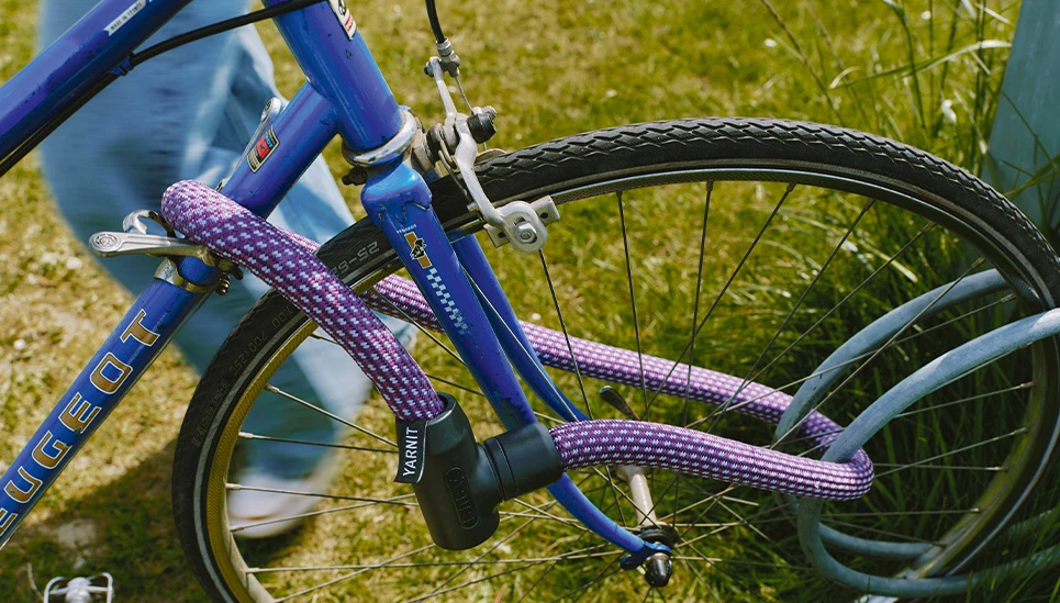 YARNIT Kettenschloss midnight purple um den Vorderreifen und Fahrradrahmen gewickelt © ABUS