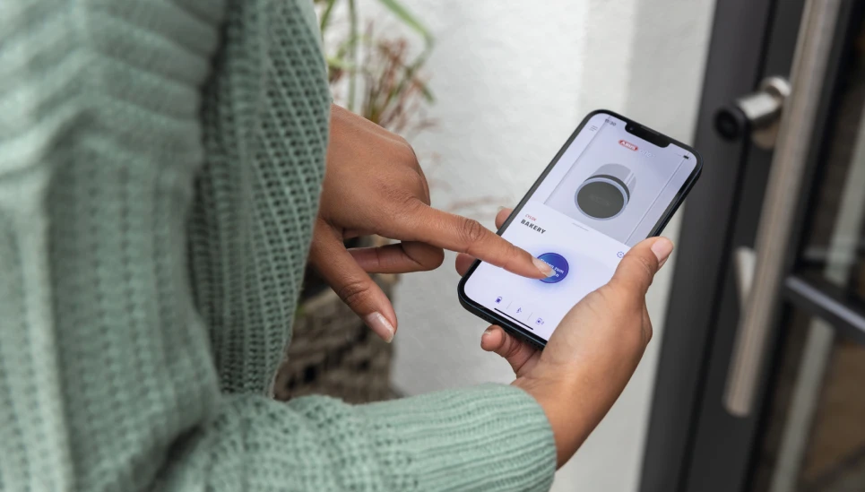 Frau öffnet per Smartphone die Eingangstür © ABUS