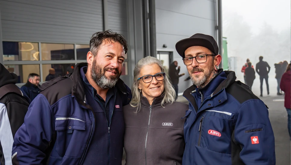 Drei Mitarbeiter in ABUS Firmenkleidung stehen eng beieinander und lächeln in die Kamera © ABUS