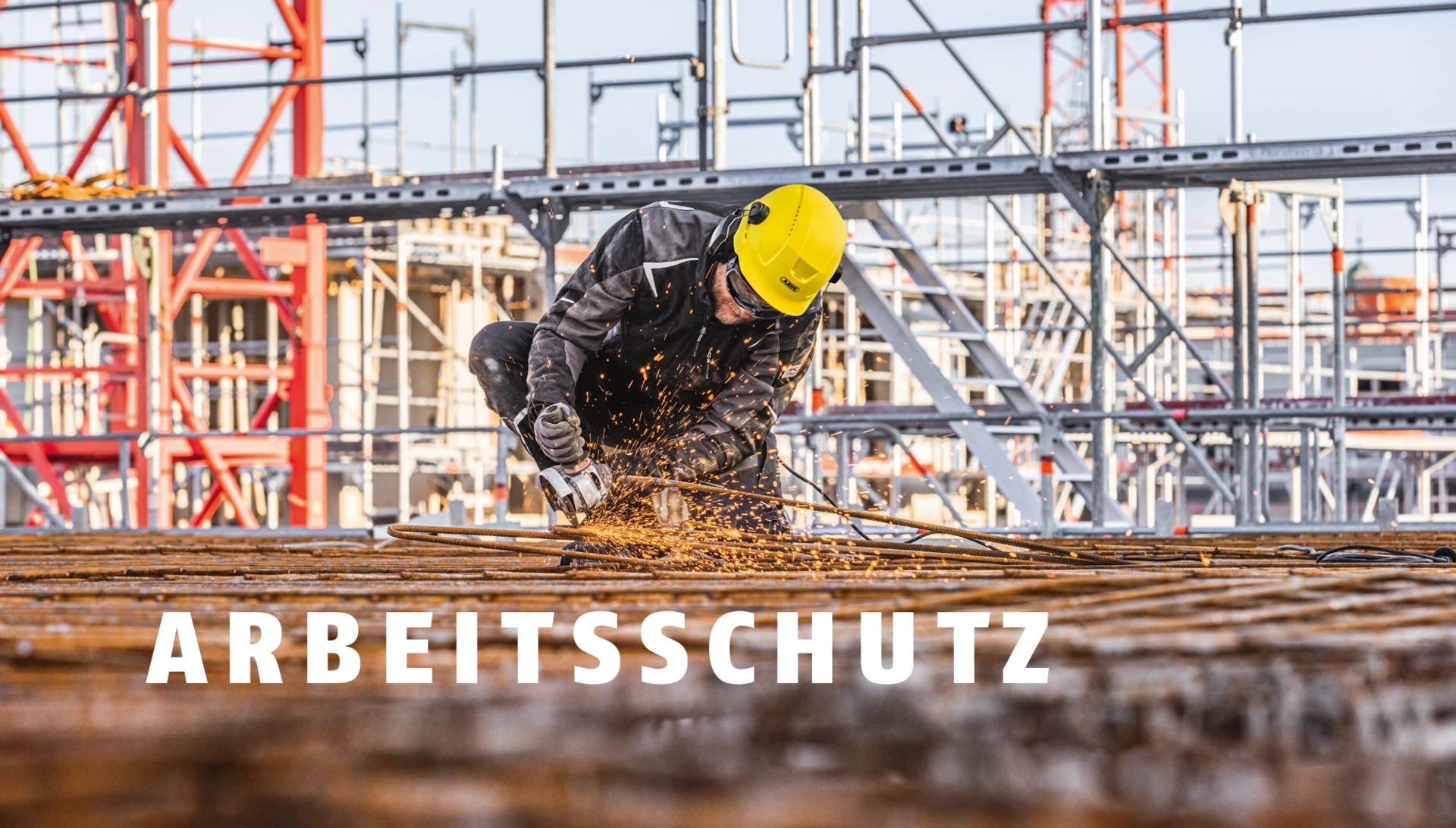 Mann mit gelbem ABUS-Helm trennt Metall mit einem Winkelschleifer auf einer Baustelle © ABUS