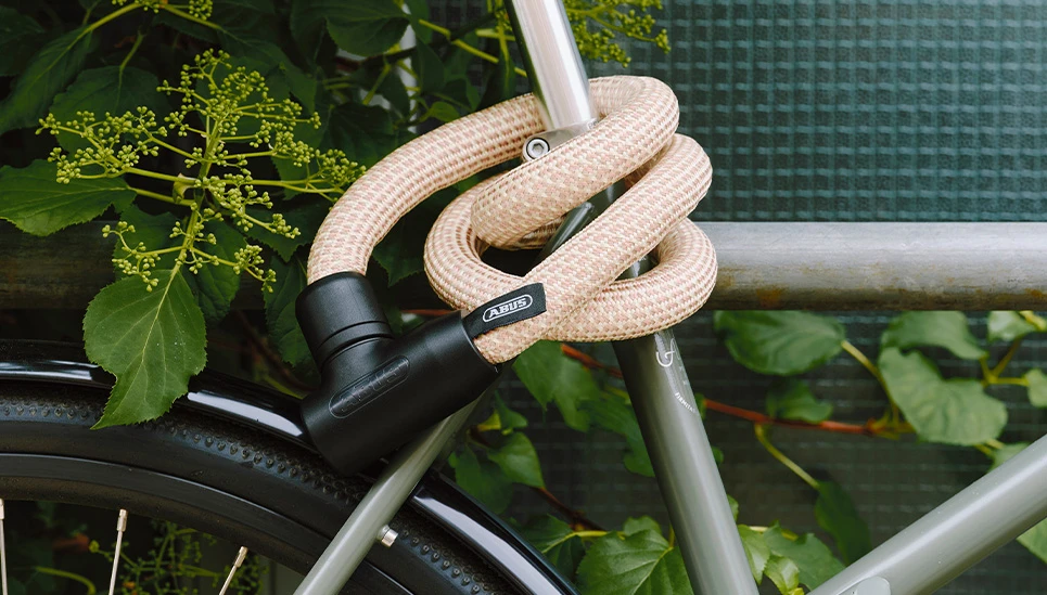 Antivol à chaîne YARNIT, couleur sable beige, solidement enroulé autour du cadre d'un vélo © ABUS