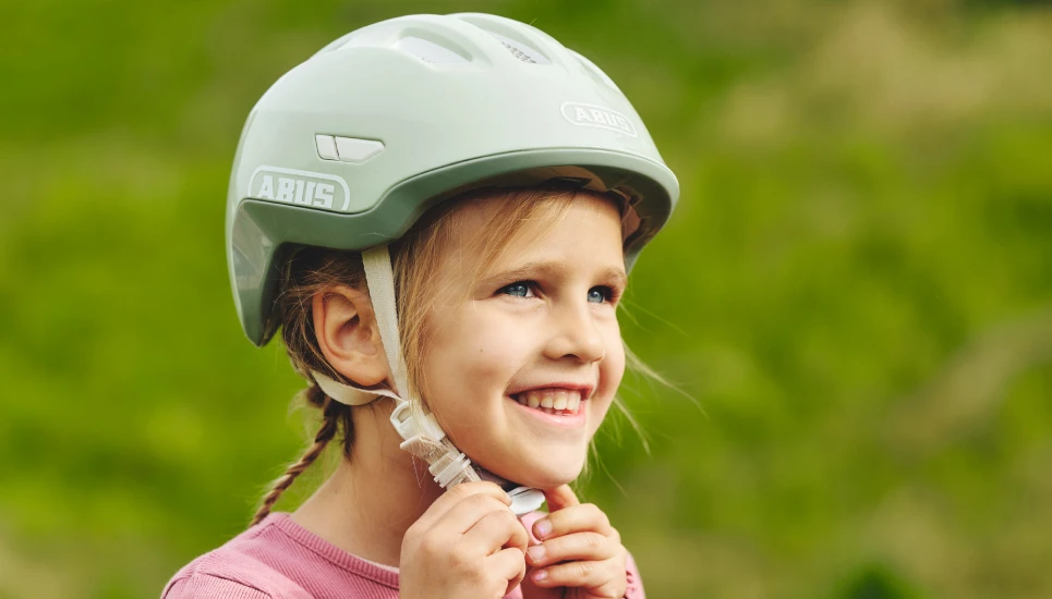 Lächelndes Mädchen beim Verschließen des Fidlocks am Kinderhelm Smiley 3.0 FL.ACE LED  © ABUS