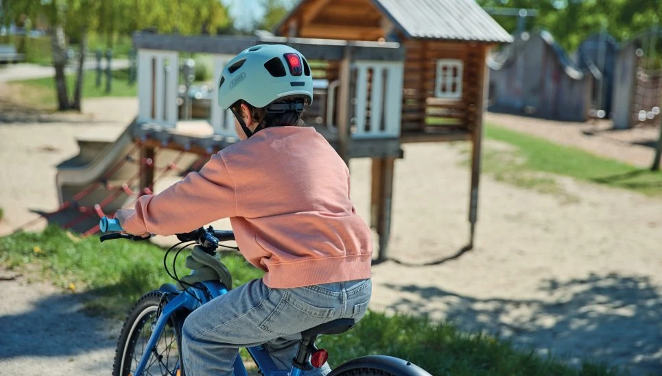 A boy rides his bike past the playground wearing a YOUN-I 3.0 powder green cycling helmet © ABUS