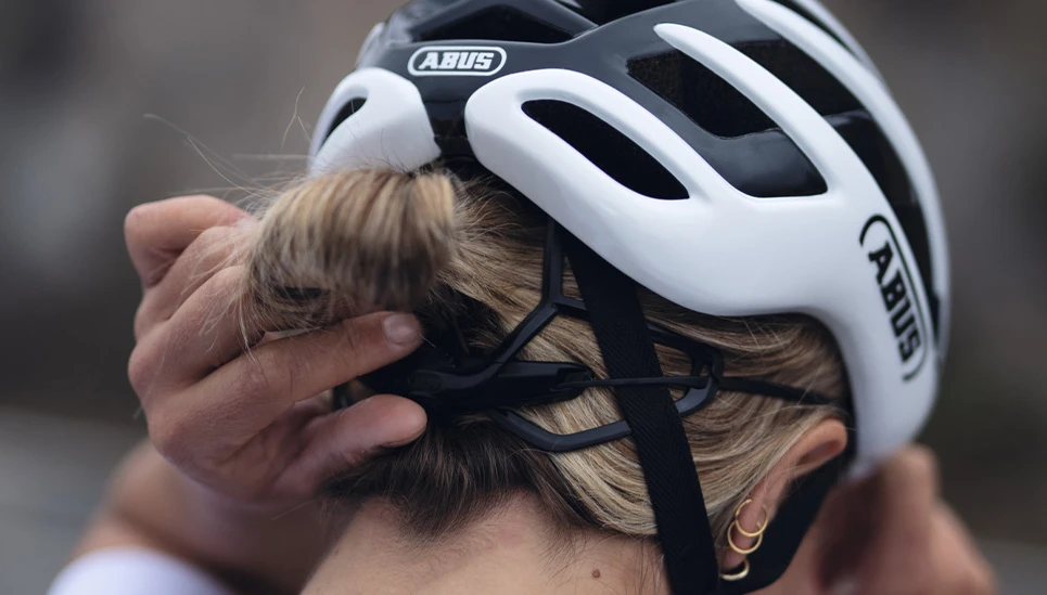 Fahrerin stellt den ABUS AirBreaker 2.0 am Verstellrad ein; sicherer Sitz über dem Dutt © ABUS