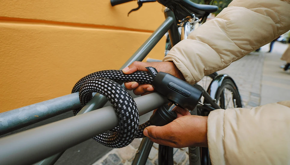 Het zwarte kettingslot van YARNIT wordt stevig om het frame van een fiets en een reling gewikkeld. © ABUS