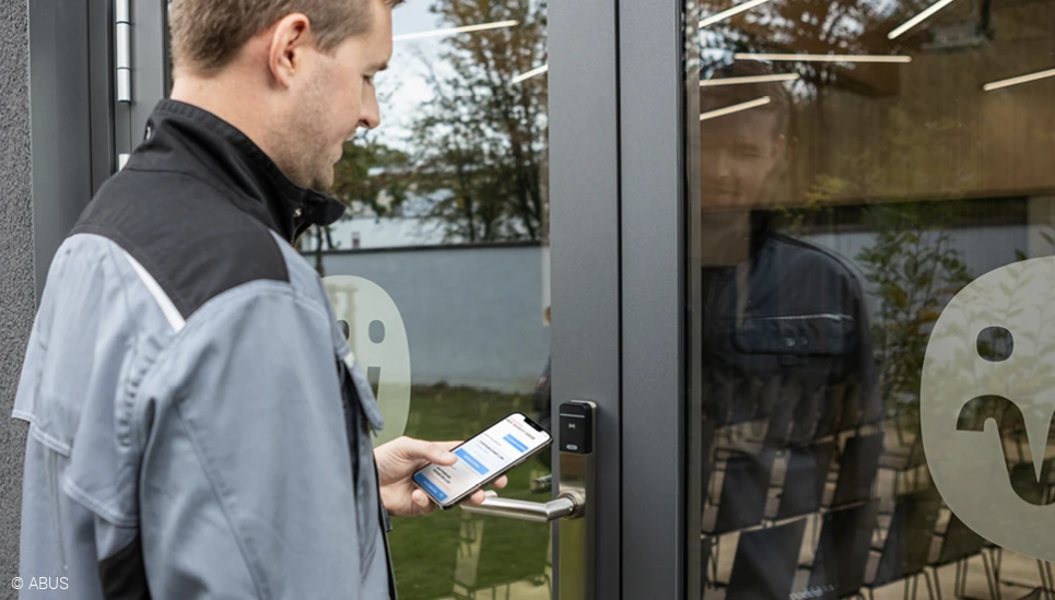 Ein Handwerker steht vor einer geschlossenen Eingangstür und blick auf das Display seines Smartphones mit der TECTIQ Admin App.