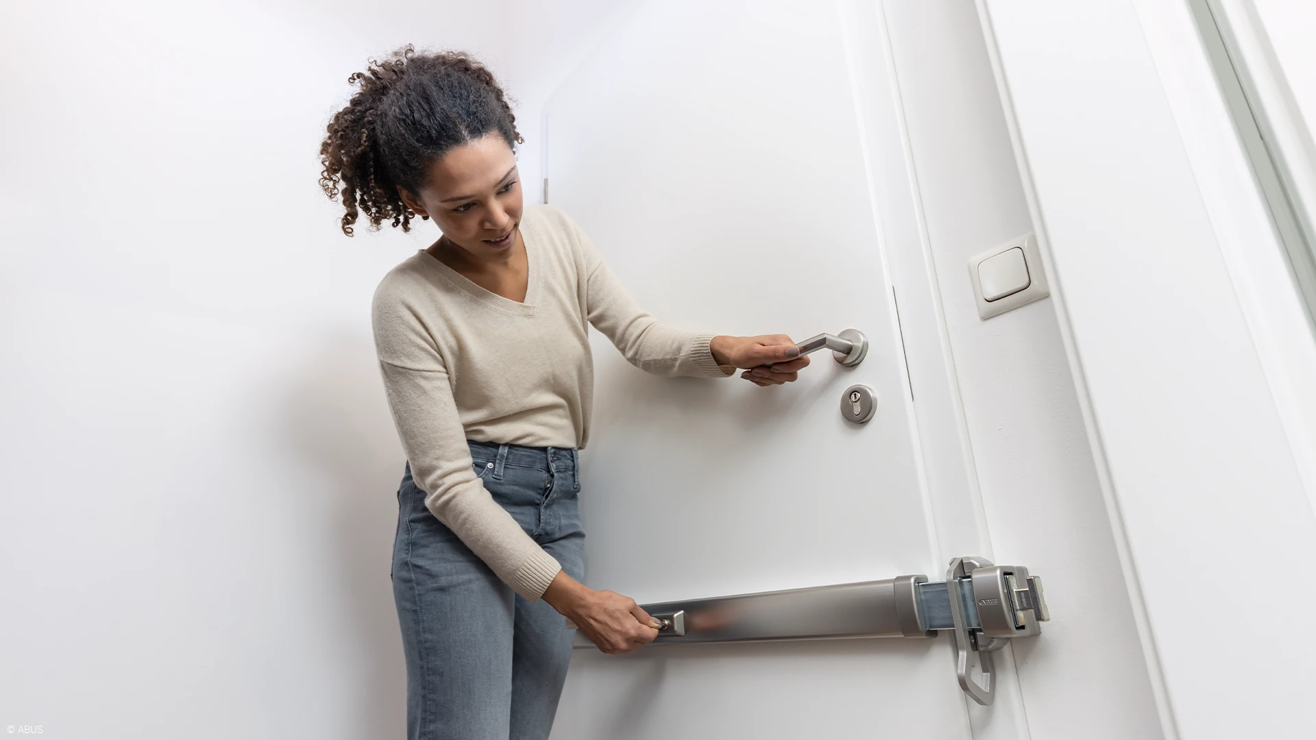 A woman locks the PR2700 security door bar with PSB2700 door guard in silver on her door © ABUS