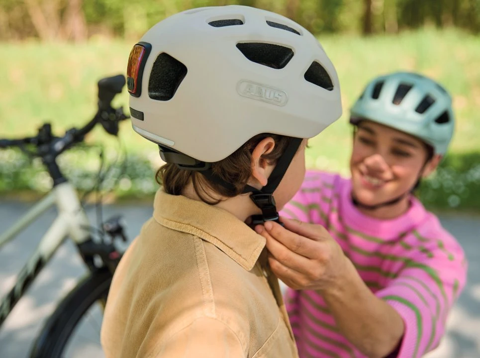 A woman fastens a boy’s cycle helmet. Both are wearing the YOUN-I 3.0 cycle helmet © ABUS