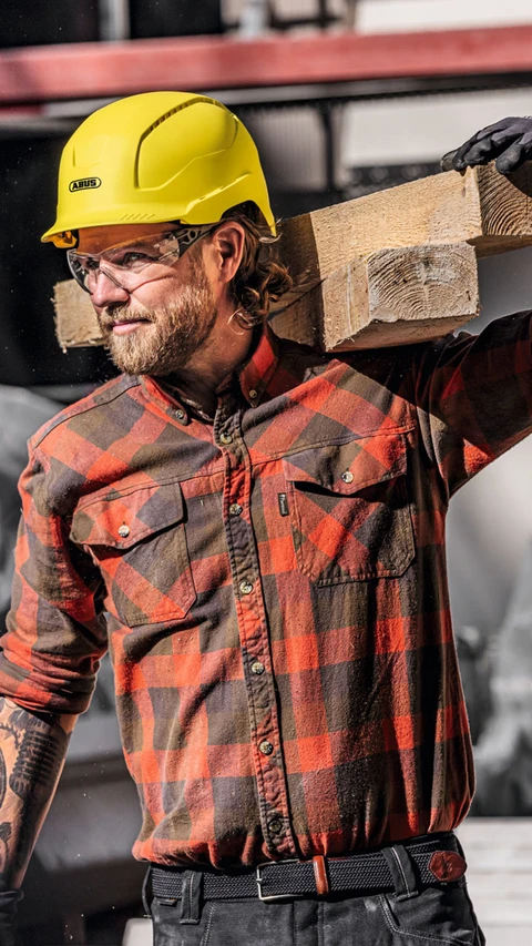 Man working on a construction site wearing a yellow Scator safety helmet and safety goggles from ABUS © ABUS