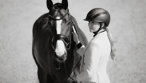 Eine Frau trägt den Reithelm AirLuxe Supreme Glam und steht neben einem Pferd.  ©ABUS