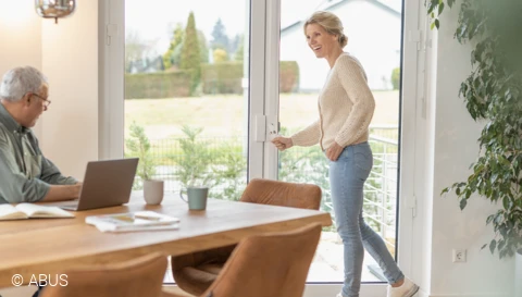 Een vrouw opent een terrasdeur die is beveiligd met het FOS650 stangslot en het FAS101 veiligheidscharnierslot © ABUS