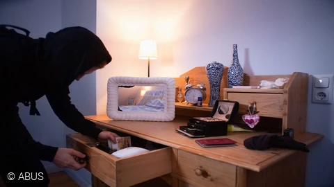 Een inbreker die zojuist geld heeft gevonden in een lade © ABUS