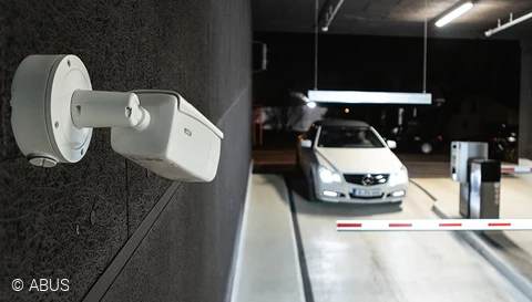 Videoüberwachungskamera in einem Parkhaus, ausgerichtet auf die Schranke. Hinter der Schranke ein weißer PKW. © ABUS