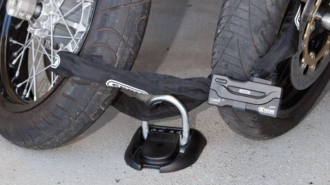 In a garage, two motorbikes are secured to a floor anchor with a chain lock on the front wheels. ©ABUS