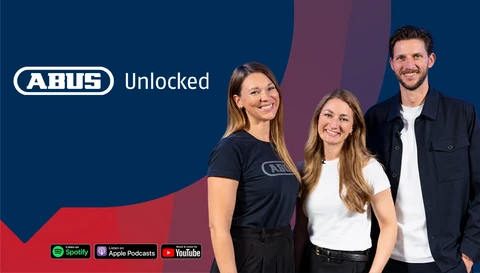 Drei lächelnde Mitarbeitende stehen vor einem dunkelblauen, roten Hintergrund. Links oben ABUS-Logo mit dem Schriftzug „Unlocked“, unten Logos von Spotify, Apple Podcasts und YouTube © ABUS