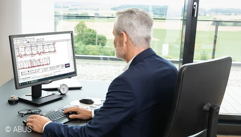 Ein Mann sitzt vor einem Monitor, auf dem ein Bauplan zu sehen ist. © ABUS