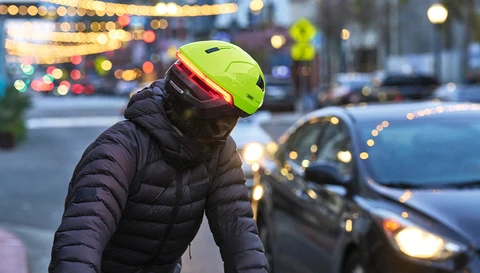 Fahrradfahrer im Straßenverkehr bei Dämmerung trägt Fahrradhelm HYP-E in signal yellow mit leuchtendem Rücklicht © ABUS