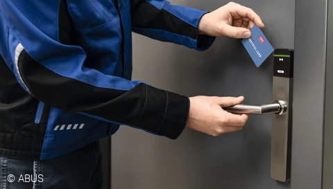 Ein Handwerker öffnet mittels einer Zutrittskarte eine Eingangstüre. © ABUS
