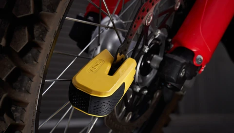 Das Vorderrad eines Motorrades ist mit einem gelben Bremsscheibenschloss mit Alarmfunktion gesichert, das an der Bremsscheibe angelegt ist. ©ABUS