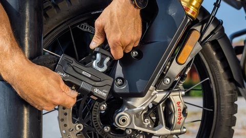 A man secures his motorbike to a lamppost with a chain lock on the front wheel. ©ABUS