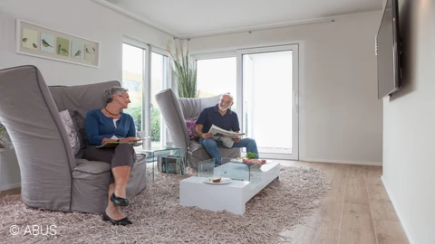 Zwei Senioren die jeweils auf einem Sessel sitzen und sich gegenseitig anlächeln © ABUS