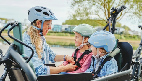 Frau trägt den urbanen Fahrradhelm XOXO während sie Kind im Lastenrad den Kinderhelm Smiley 3.0 blue whale einstellt © ABUS