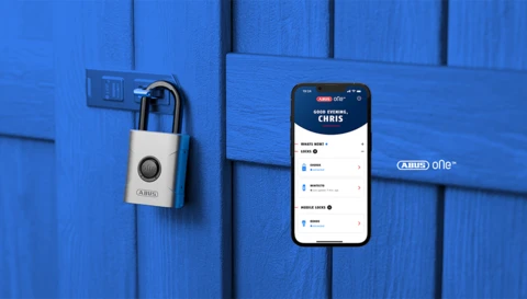 Cadenas intelligent EVEROX One sur une porte de hangar en bois et un smartphone avec écran d'application au premier plan © ABUS