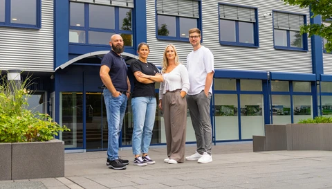 Vier Mitarbeitende der ABUS KG stehen vor dem Firmengebäude am Standort Rehe und blicken in die Kamera © ABUS